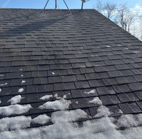Snow-dusted dark shingle roof under a clear winter sky
