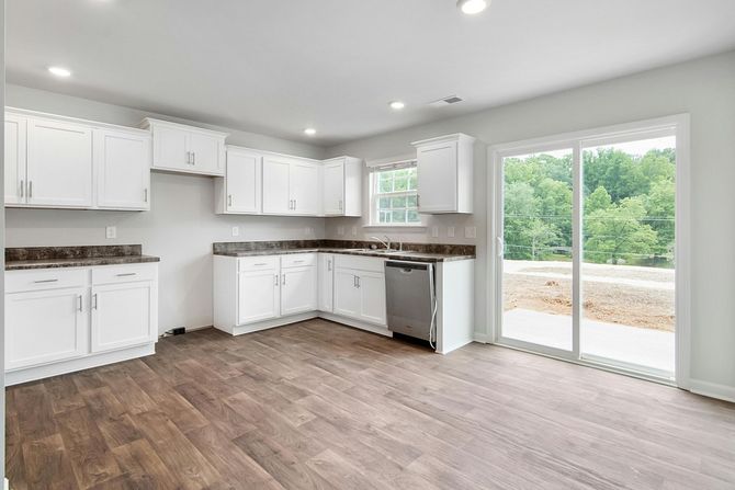 White kitchen with cabinets, stainless steel appliances, and sliding glass door overlooking trees.