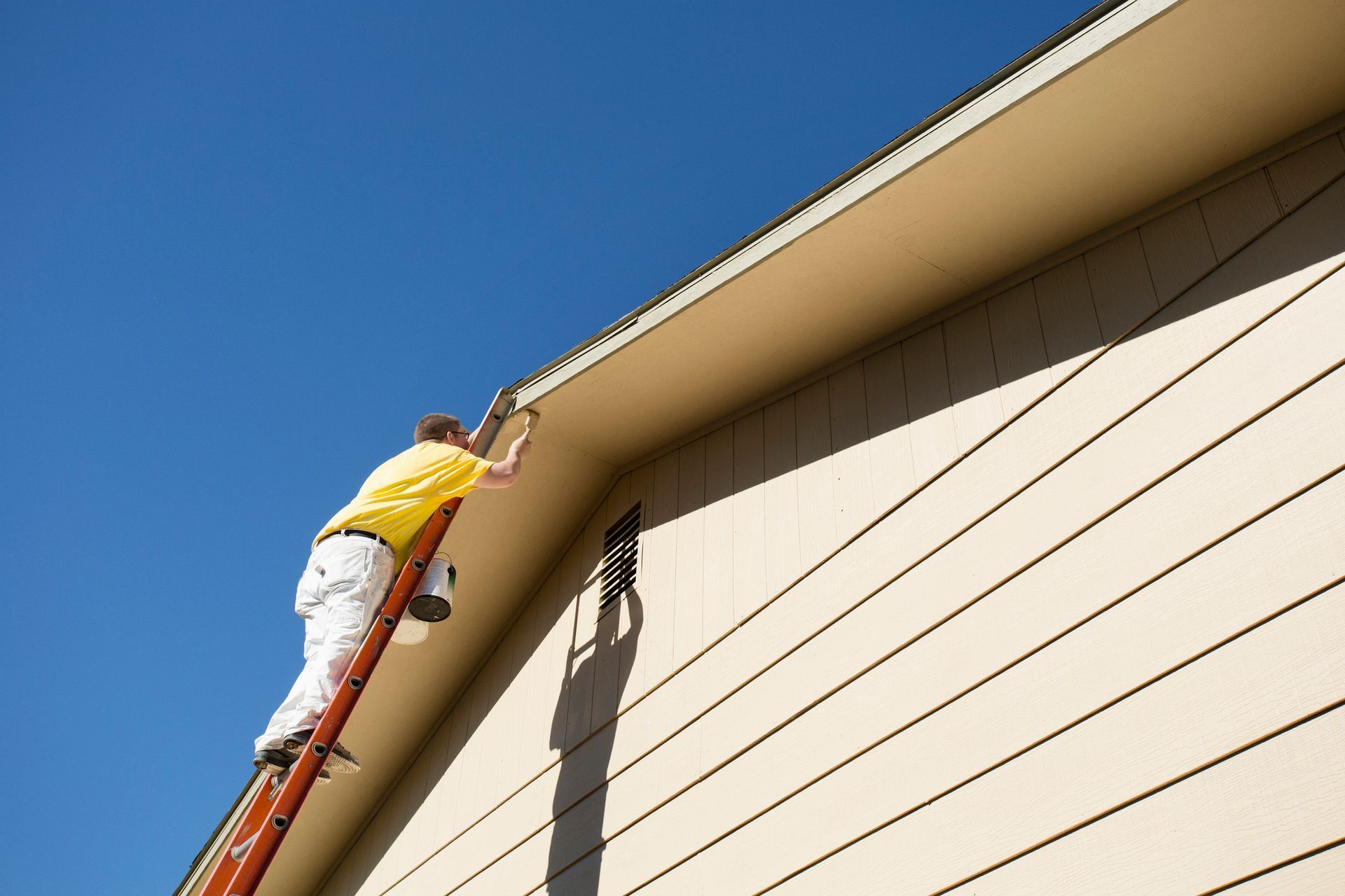 A man on a ladder paints the side of a house
