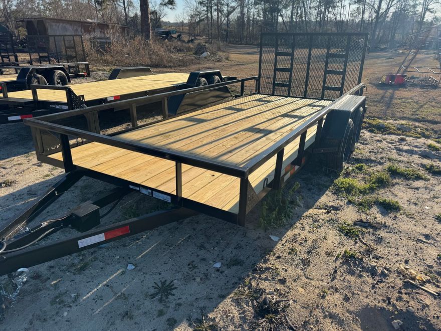 Two black metal utility trailers with new wooden floorboards sitting in a gravel lot on a sunny day.
