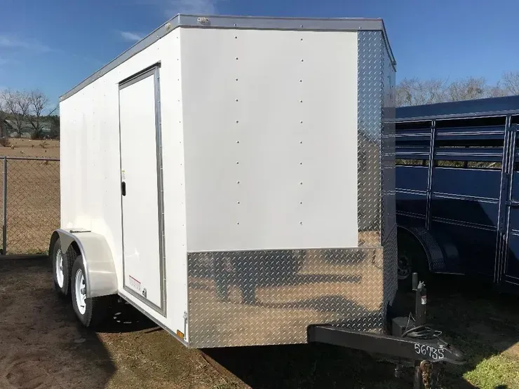 Woman in straw hat smiles, holding wine glass near a lake.