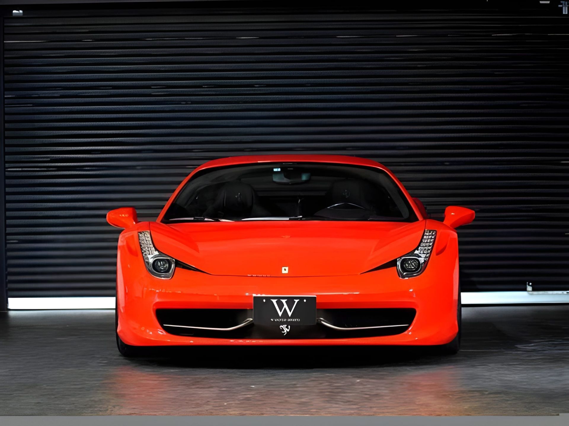 Front view of a bright orange Ferrari sports car parked in front of a dark, closed garage door.