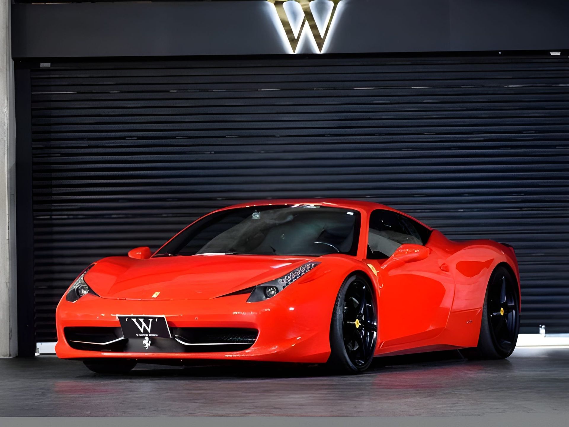 Front view of a bright orange Ferrari sports car parked in front of a dark, closed garage door.