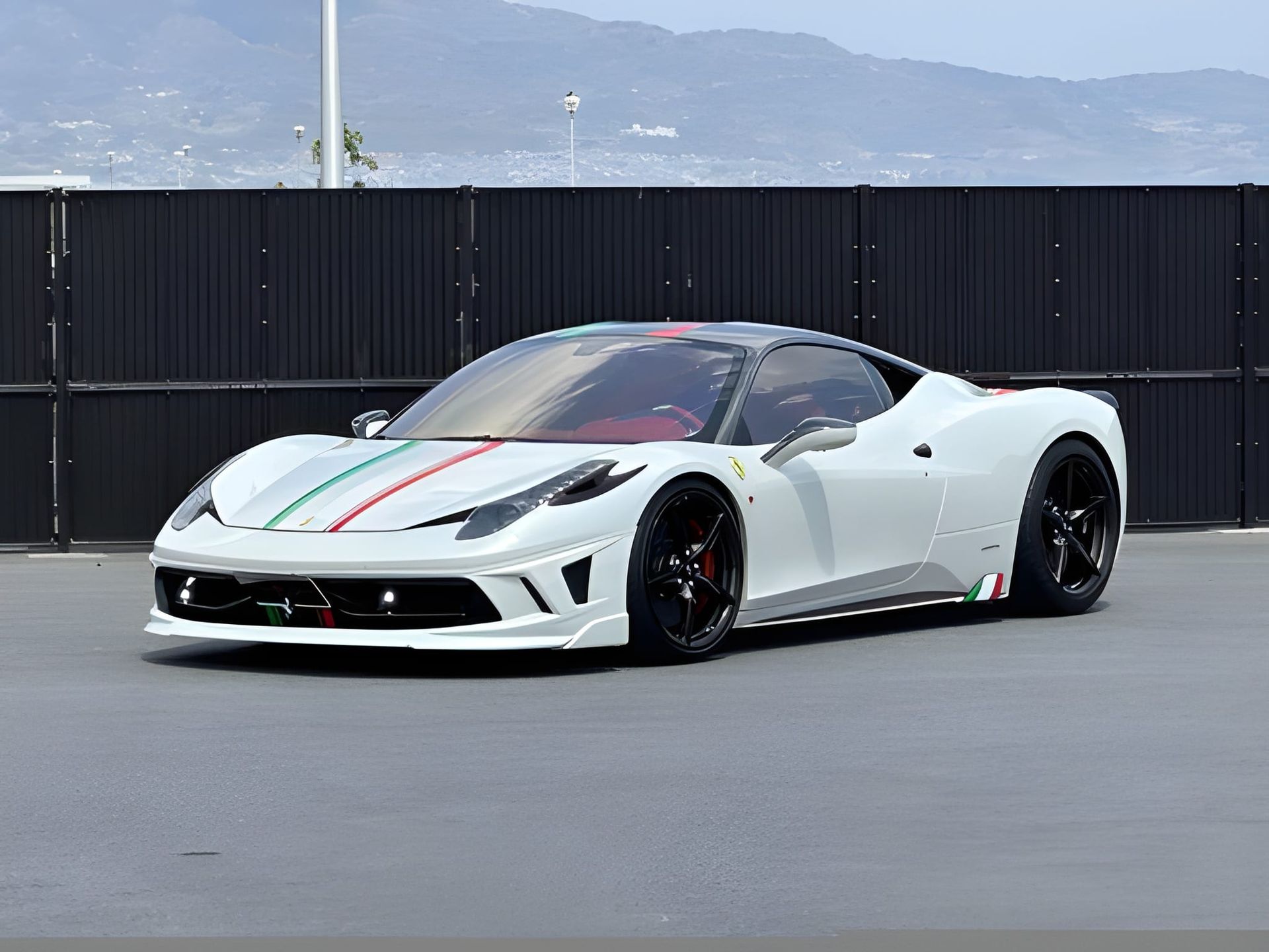 White Ferrari 458 with Italian flag stripes on hood, parked in front of a dark fence.