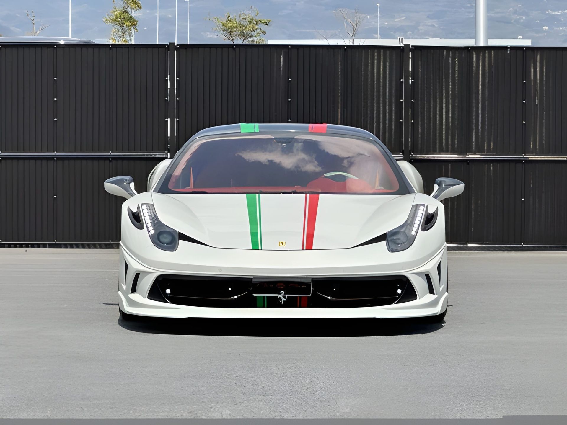 White Ferrari 458 with Italian flag stripes on hood, parked in front of a dark fence.