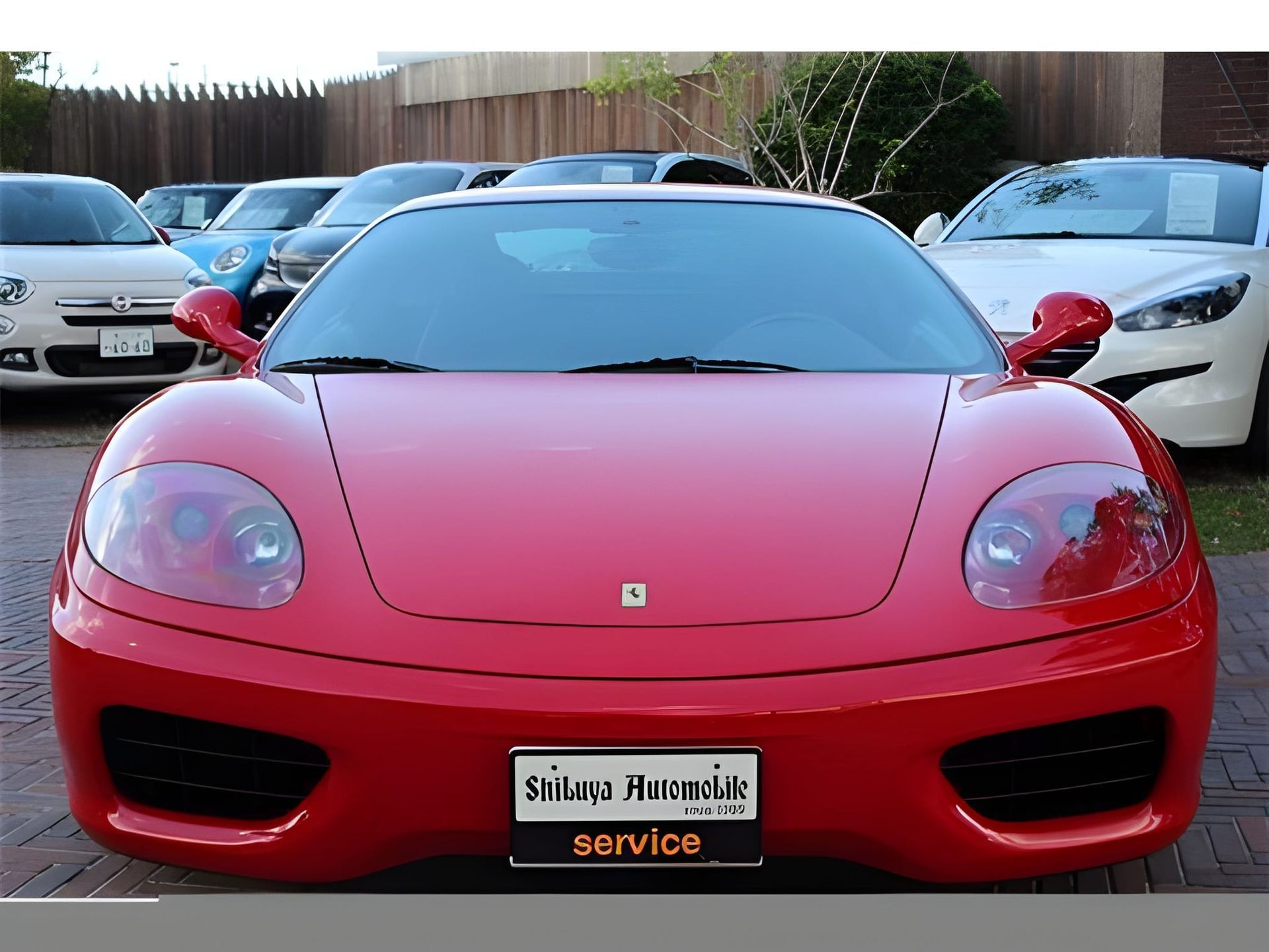 Red Ferrari sports car parked in front of other cars, likely a dealership.