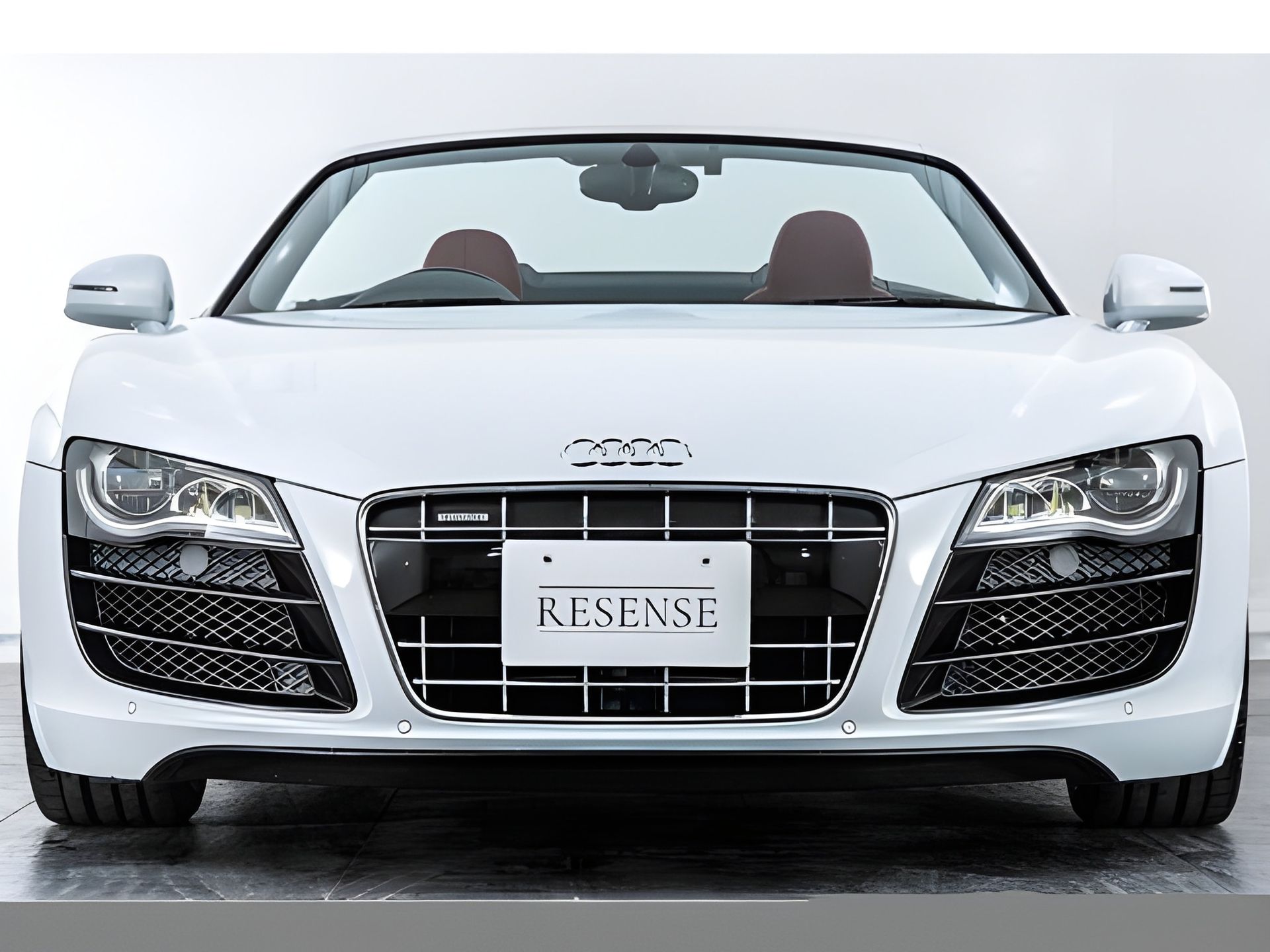 White Audi R8 Spyder convertible, front view. Black grille, brown interior. "RESENSE" license plate.