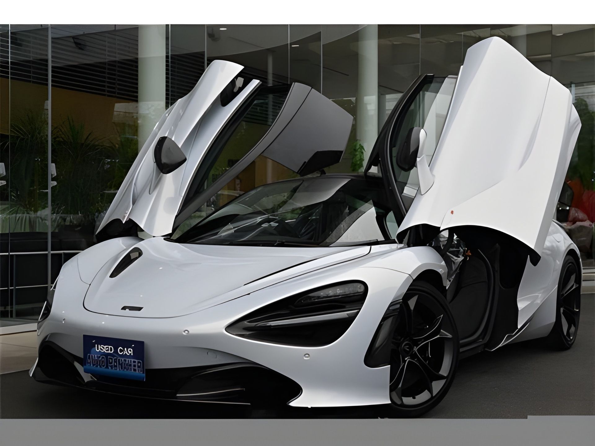 Silver McLaren sports car with black accents, parked in front of a building, displaying a