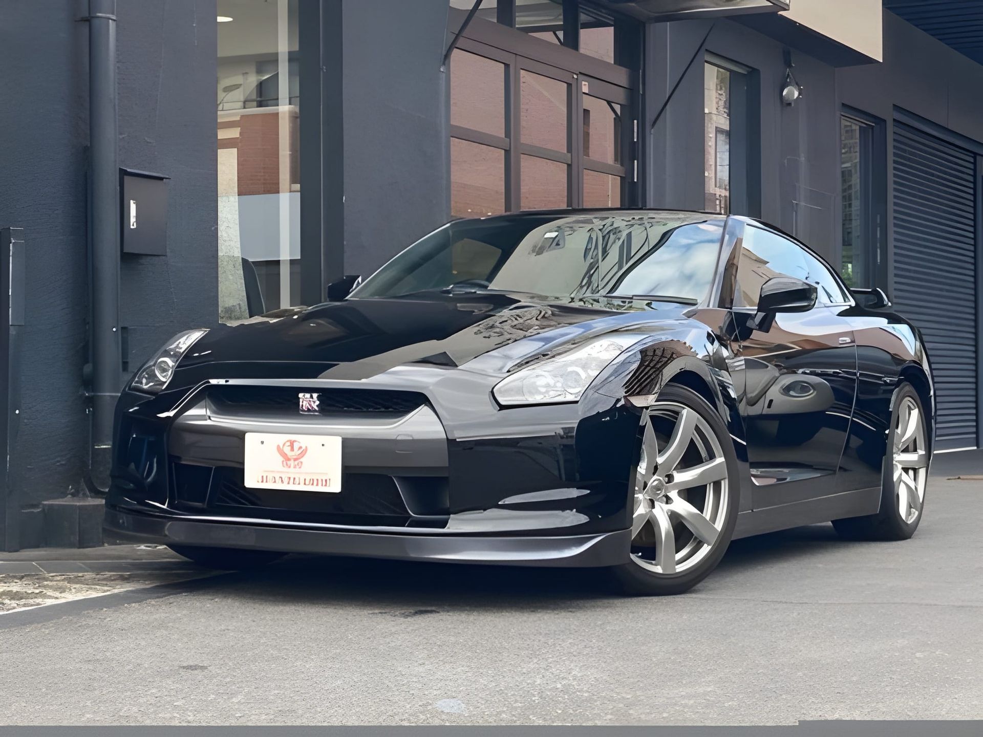 Black Nissan GT-R sports car parked in front of a building; front view showing hood scoop, grill, and headlights.