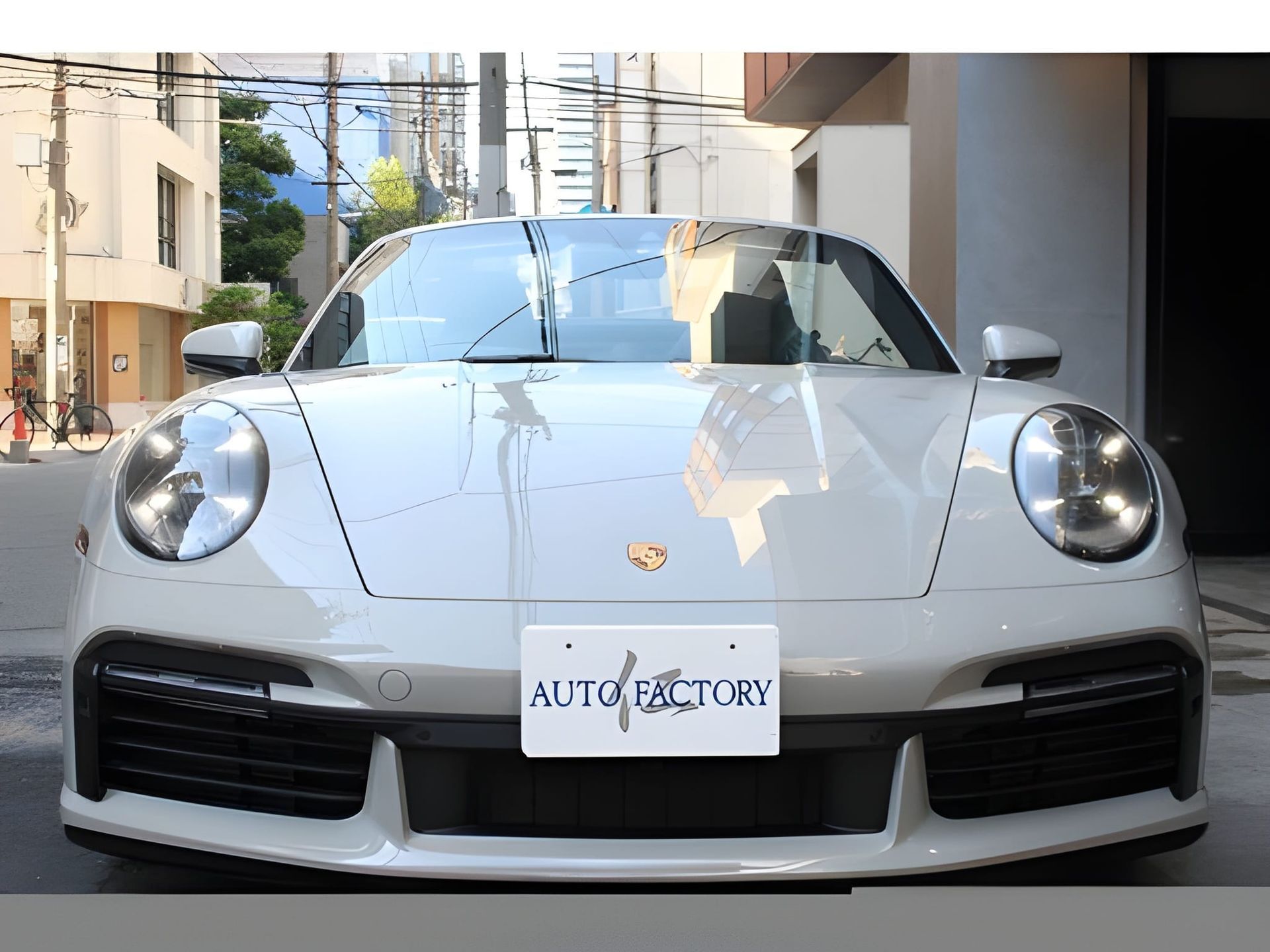 White Porsche 911 parked on a city street; front view with license plate "AUTO FACTORY".