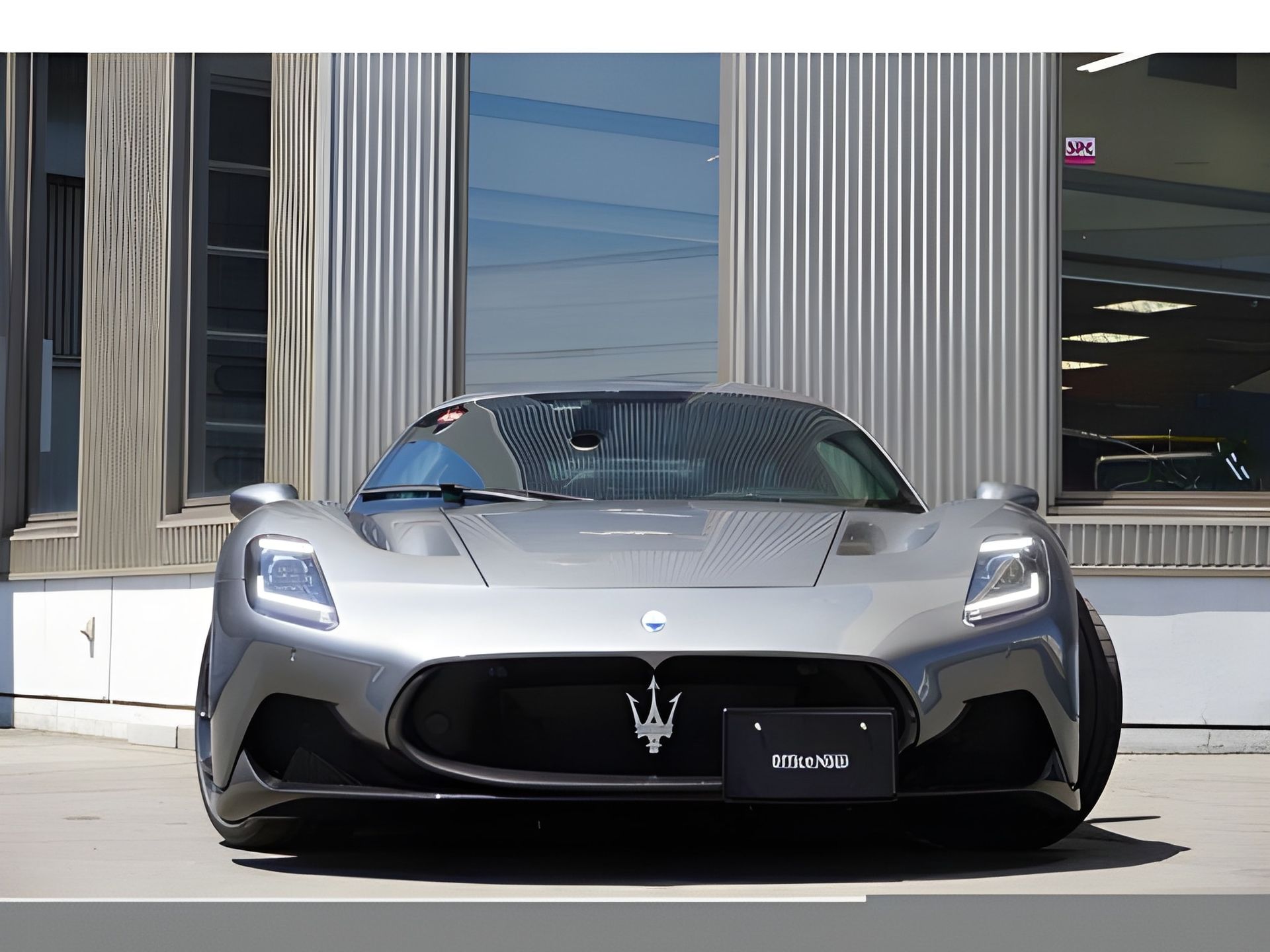 Gray Maserati MC20 sports car parked in front of a modern building with large windows.