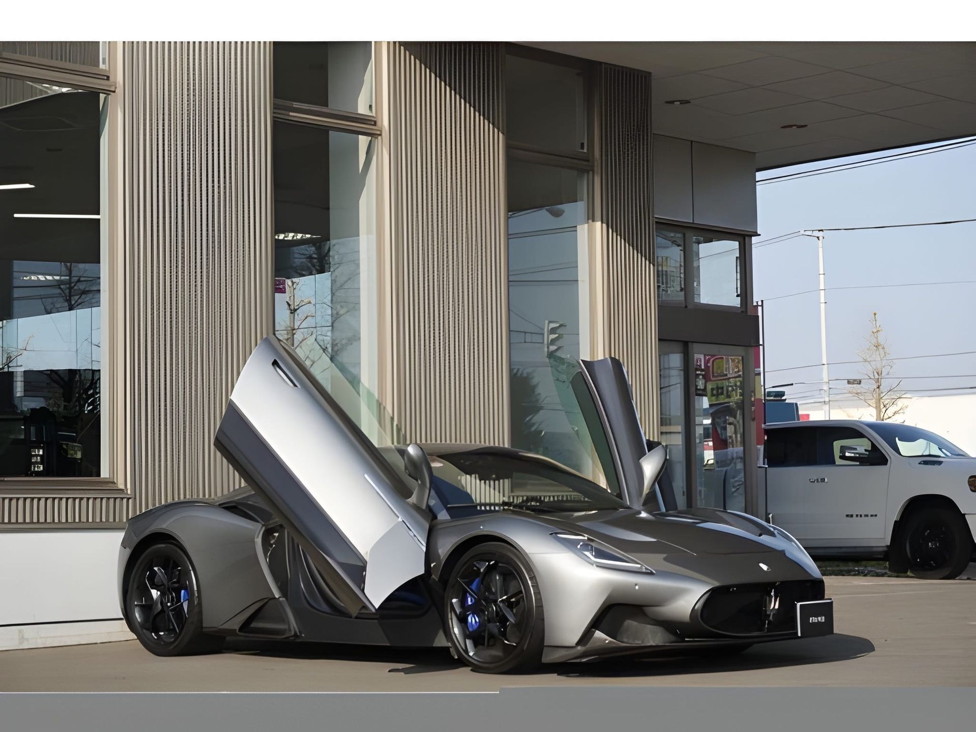 Gray Maserati MC20 sports car parked in front of a modern building with large windows.