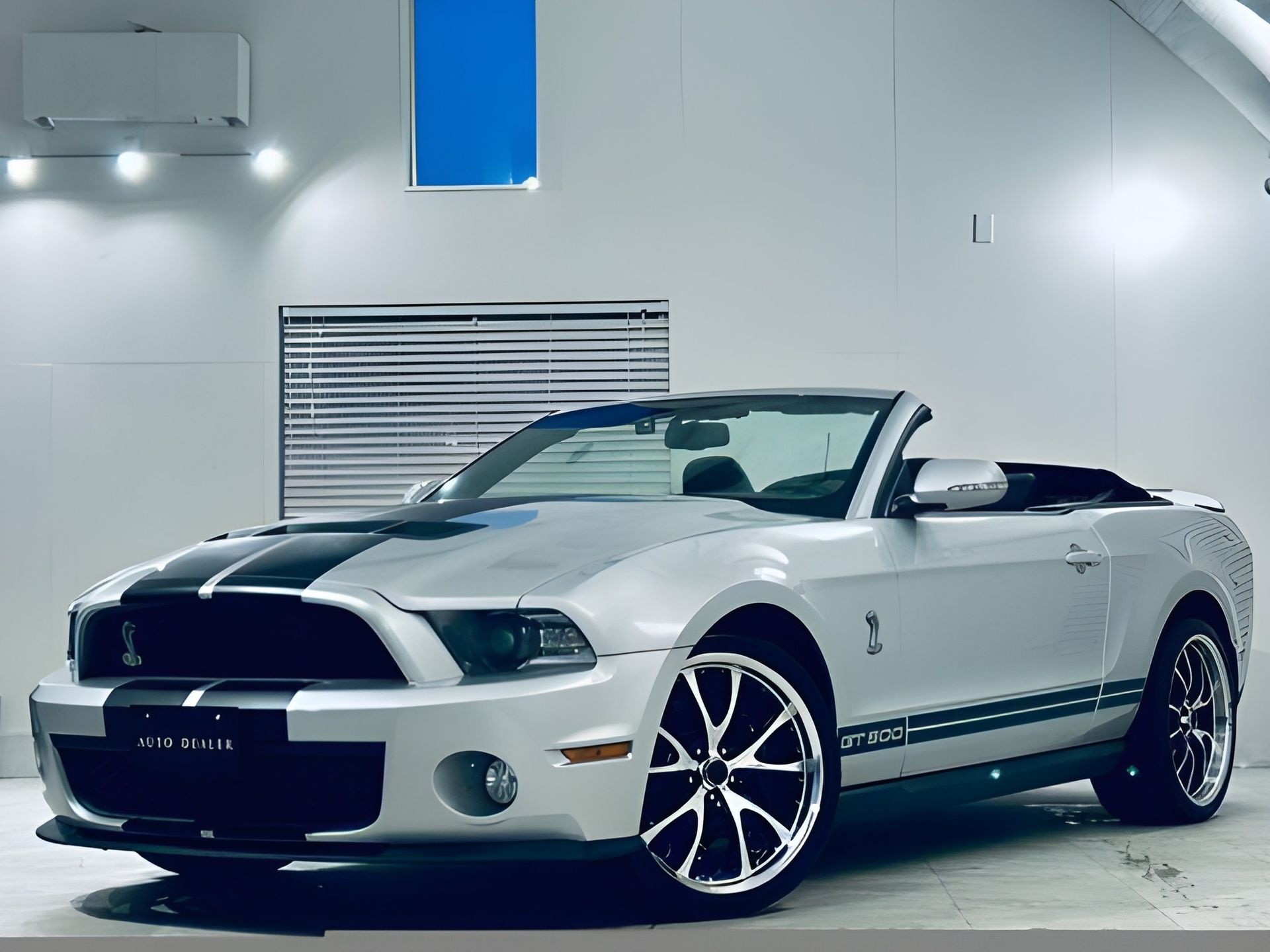 Silver Ford Shelby Mustang with black racing stripes, parked in a showroom.
