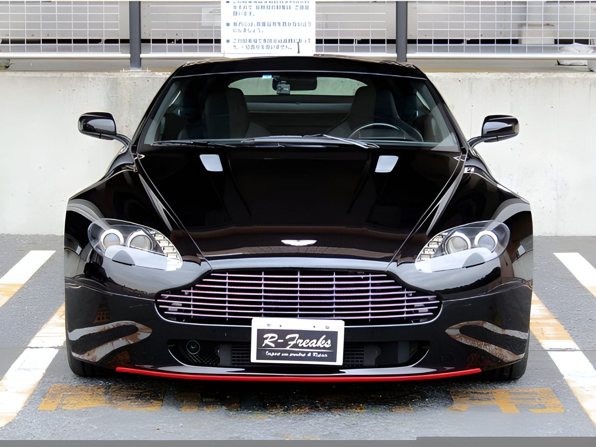 Black Aston Martin sports car parked in front of a building, red accent on the front bumper.
