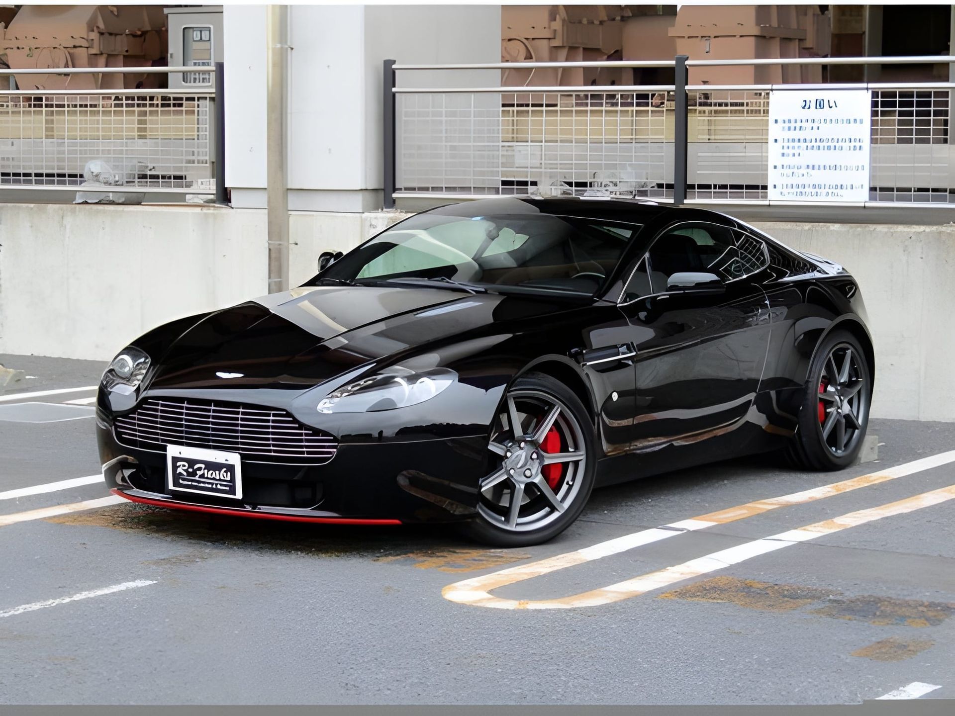 Black Aston Martin sports car parked in front of a building, red accent on the front bumper.
