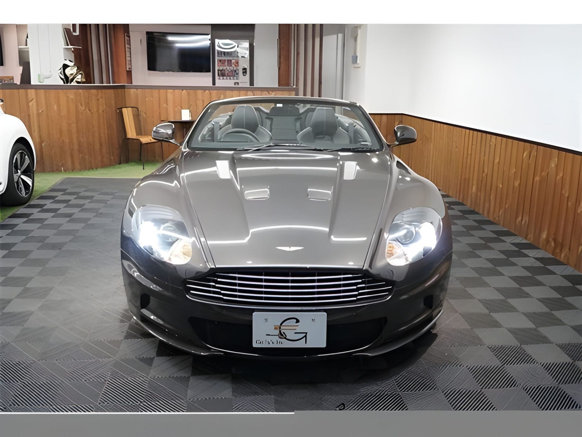 Gray Aston Martin convertible, front view, inside a showroom.