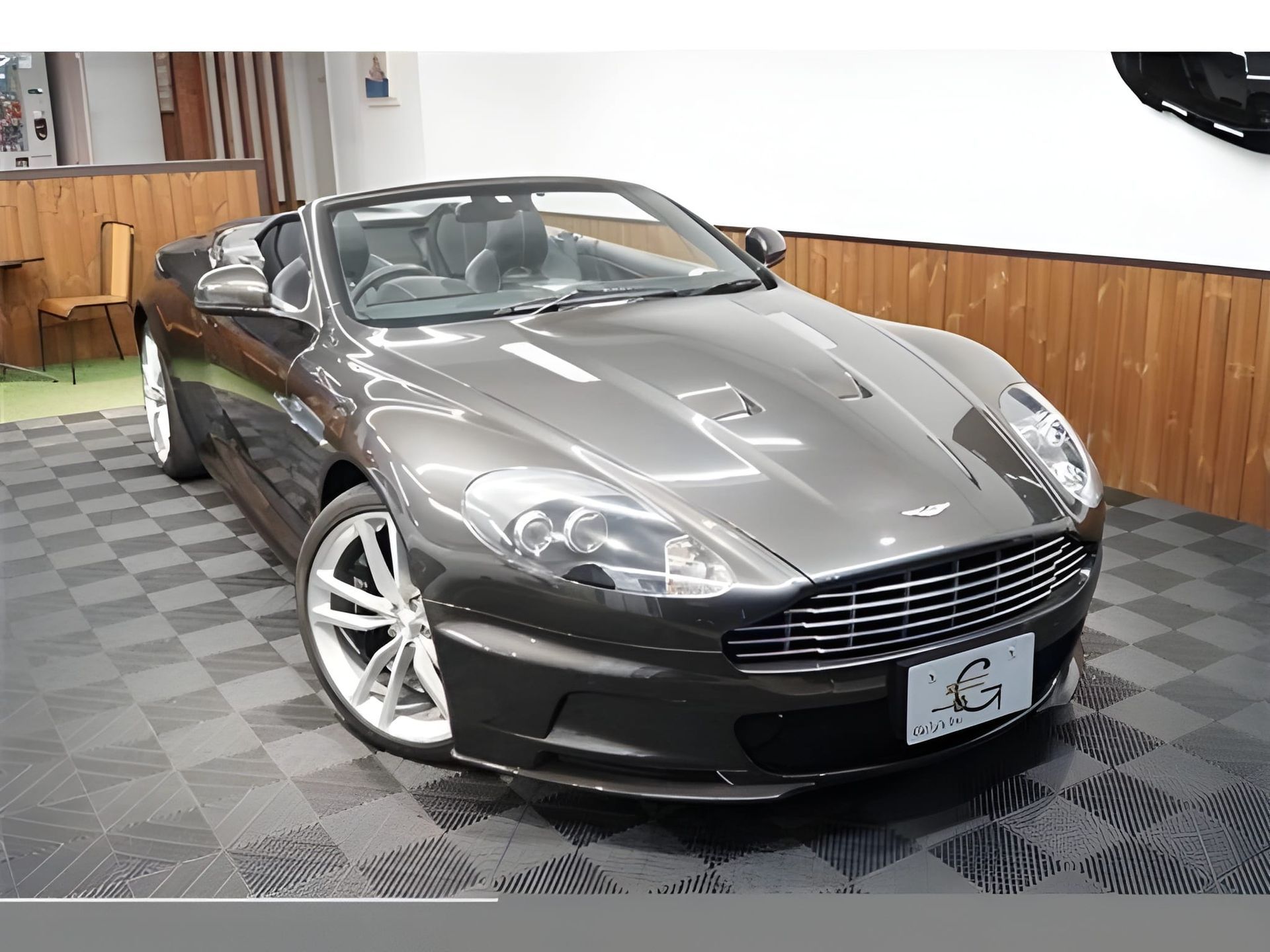 Gray Aston Martin convertible, front view, inside a showroom.