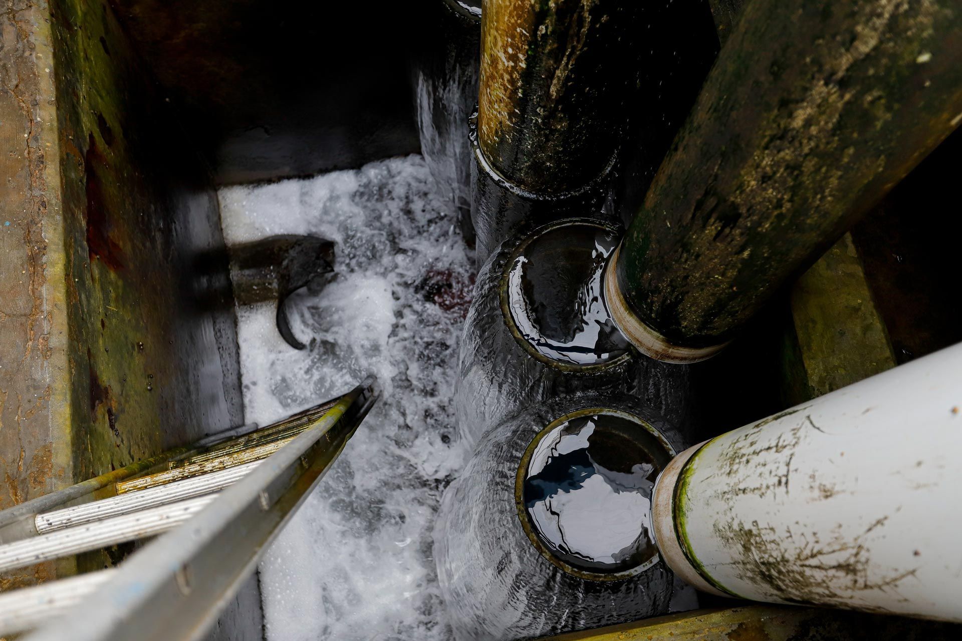 Industrial drain pipe discharging wastewater into sewer during lift station maintenance process.