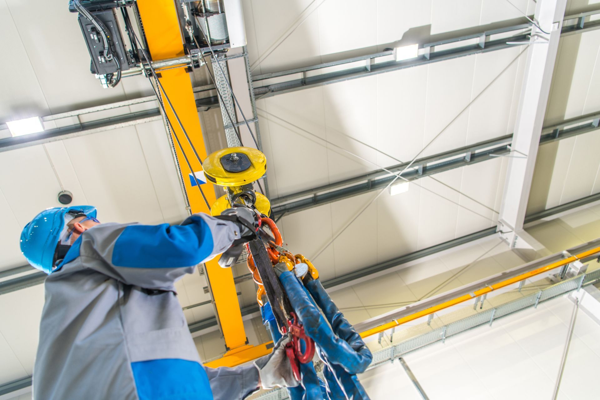 Worker operating overhead crane hoist system in industrial facility for heavy lifting safety.