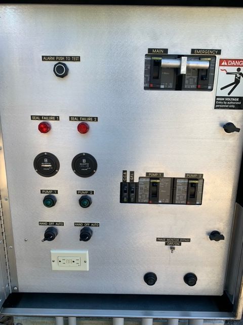 Lift station control panel with switches, indicators, and pump controls inside a metal cabinet.