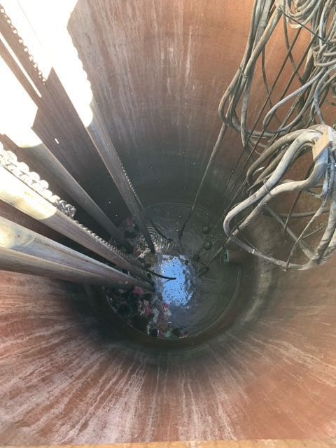 Looking down into a lift station wet well with pumps, guide rails, cables, and standing water.