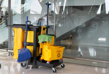 Cleaning cart with yellow buckets, broom, and mop against a glass wall.