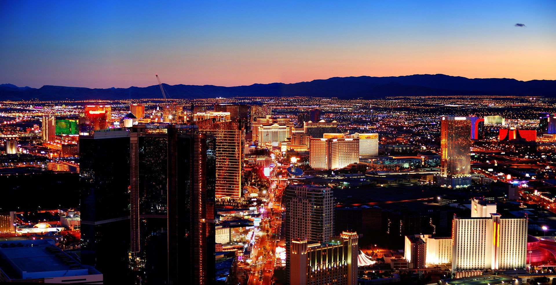 Night view of Las Vegas skyline with brightly lit hotels and casinos, dark silhouettes of buildings, and a twilight sky.