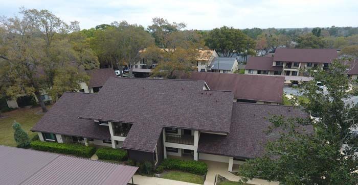 An aerial view of a large house with a brown roof surrounded by trees.