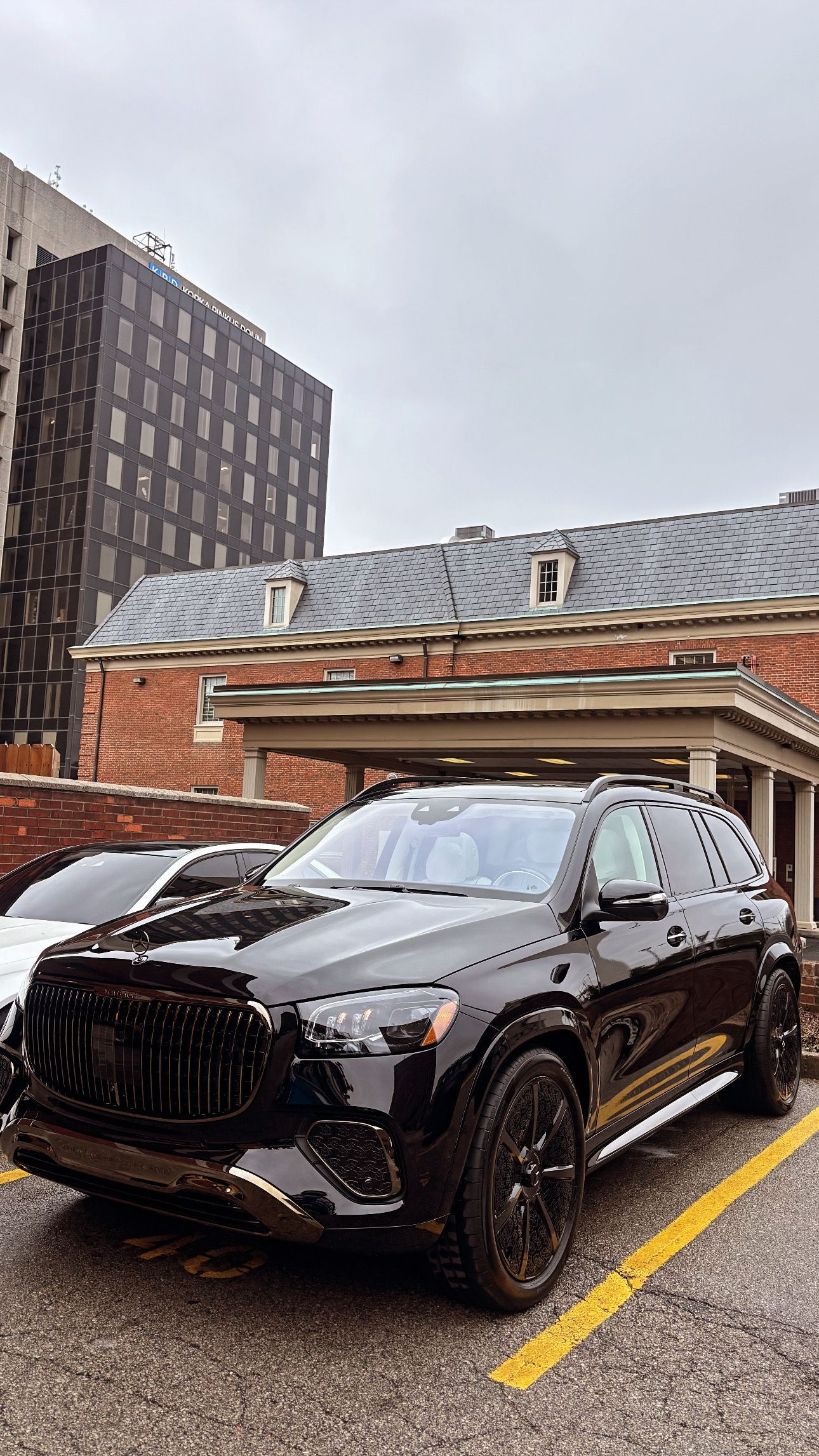 A sleek black SUV parked in an outdoor lot next to a brick building with a gray, wavy roof under an overcast sky.