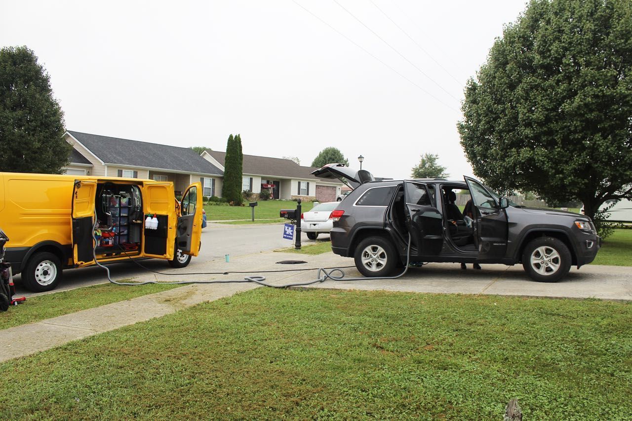 A yellow work van and a dark SUV with open doors are parked on a residential street.