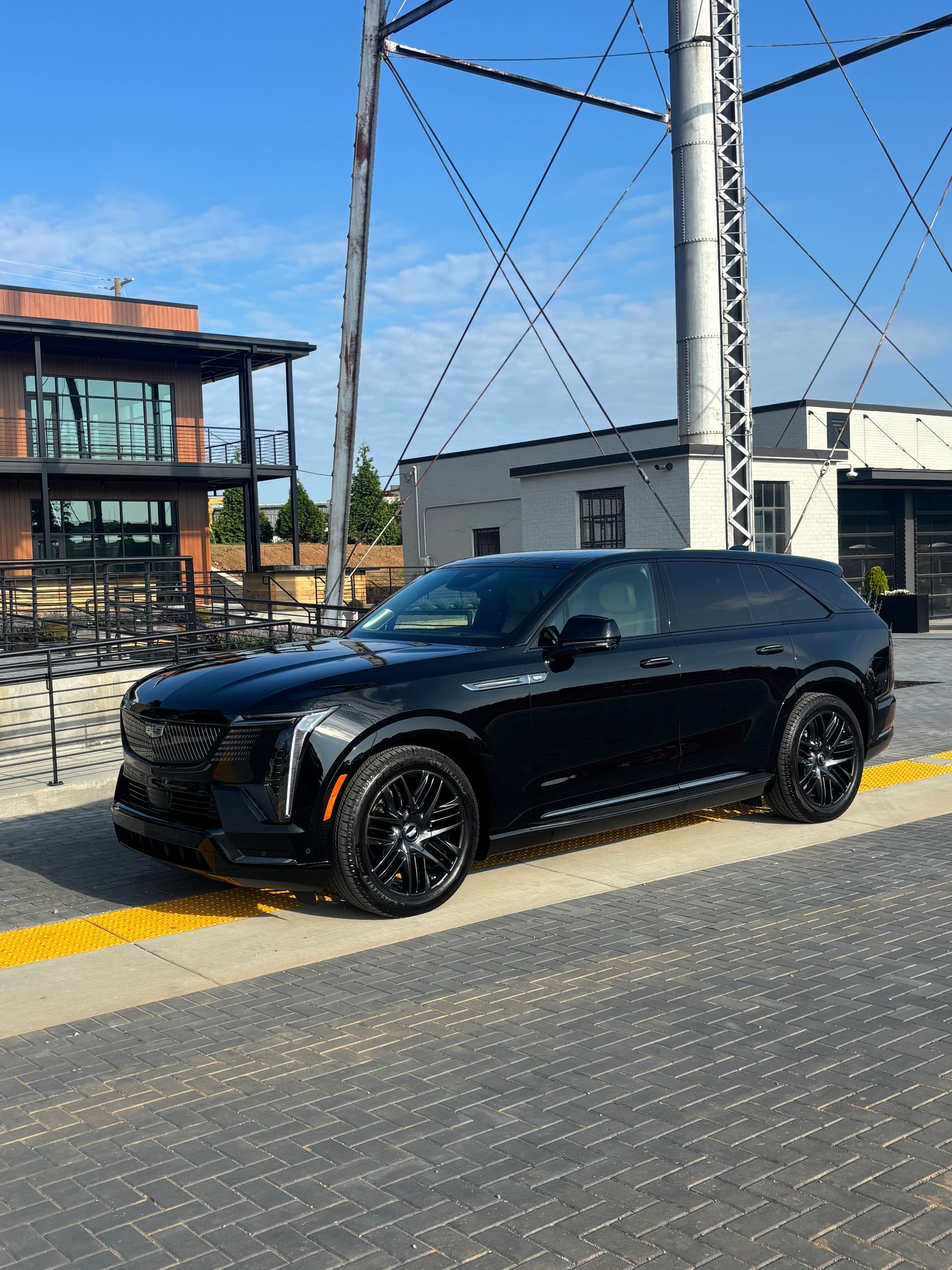 A black Cadillac SUV parked on a paved lot with a metal water tower and industrial-style buildings in the background.