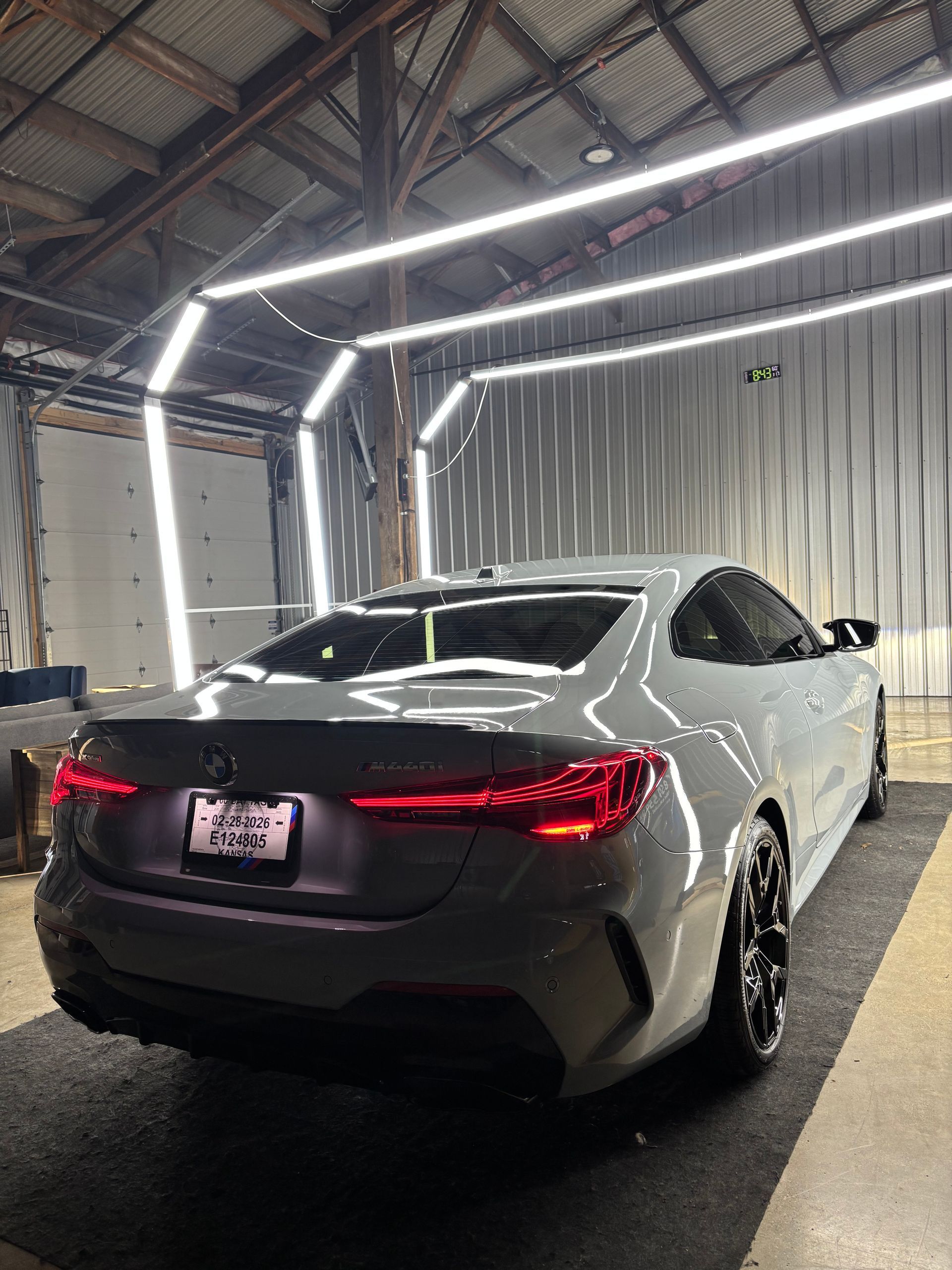 A gray BMW coupe parked in a well-lit detailing garage with bright LED overhead lights.
