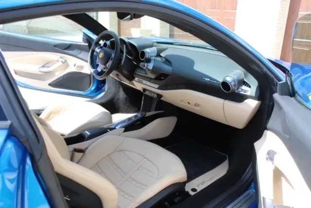 The interior of a blue car, featuring tan leather seats and a black dashboard with a prominent steering wheel.