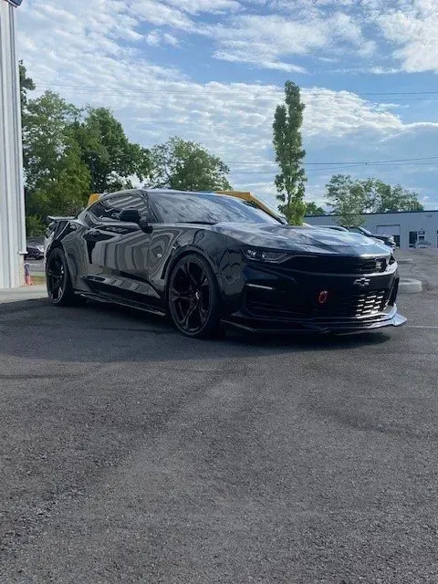 A black Chevrolet Camaro parked on asphalt under a blue, cloudy sky, seen from a front-quarter angle.