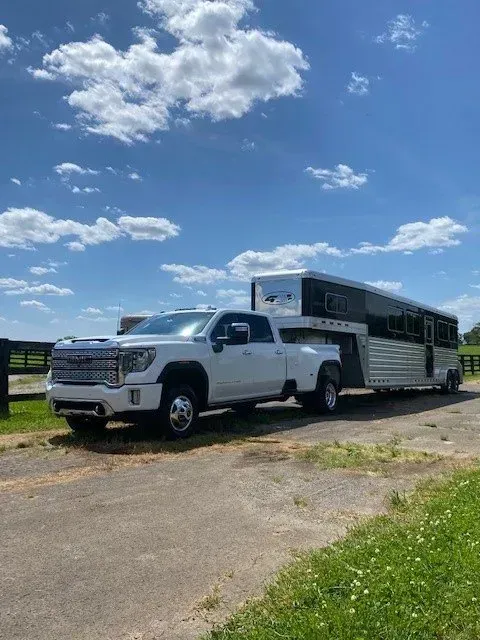 A white GMC heavy-duty pickup truck with a dual-rear-wheel configuration hauling a horse trailer on a sunny day.
