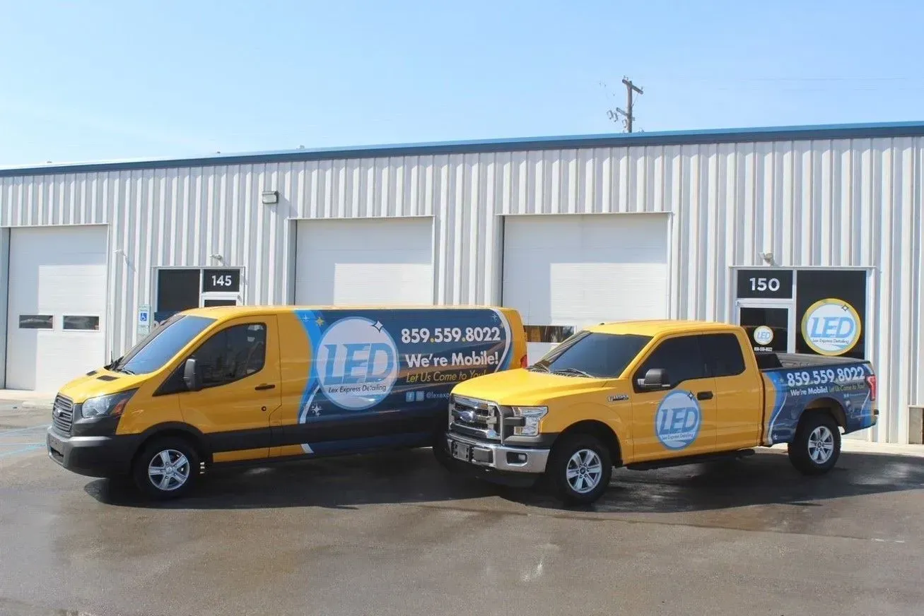 Two yellow LED Electric service vehicles parked in front of a metal warehouse building.