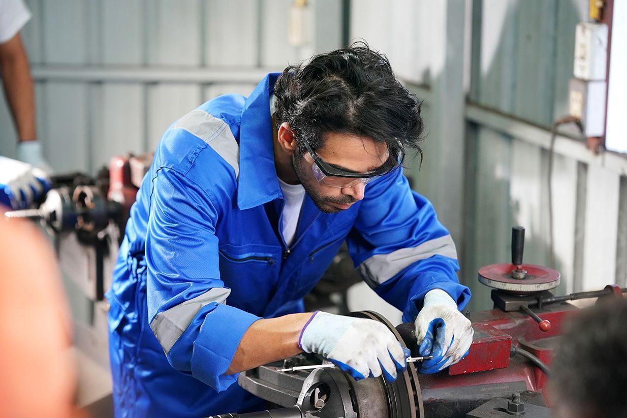 Worker in blue coveralls using a tool on a metal part in an industrial workshop.