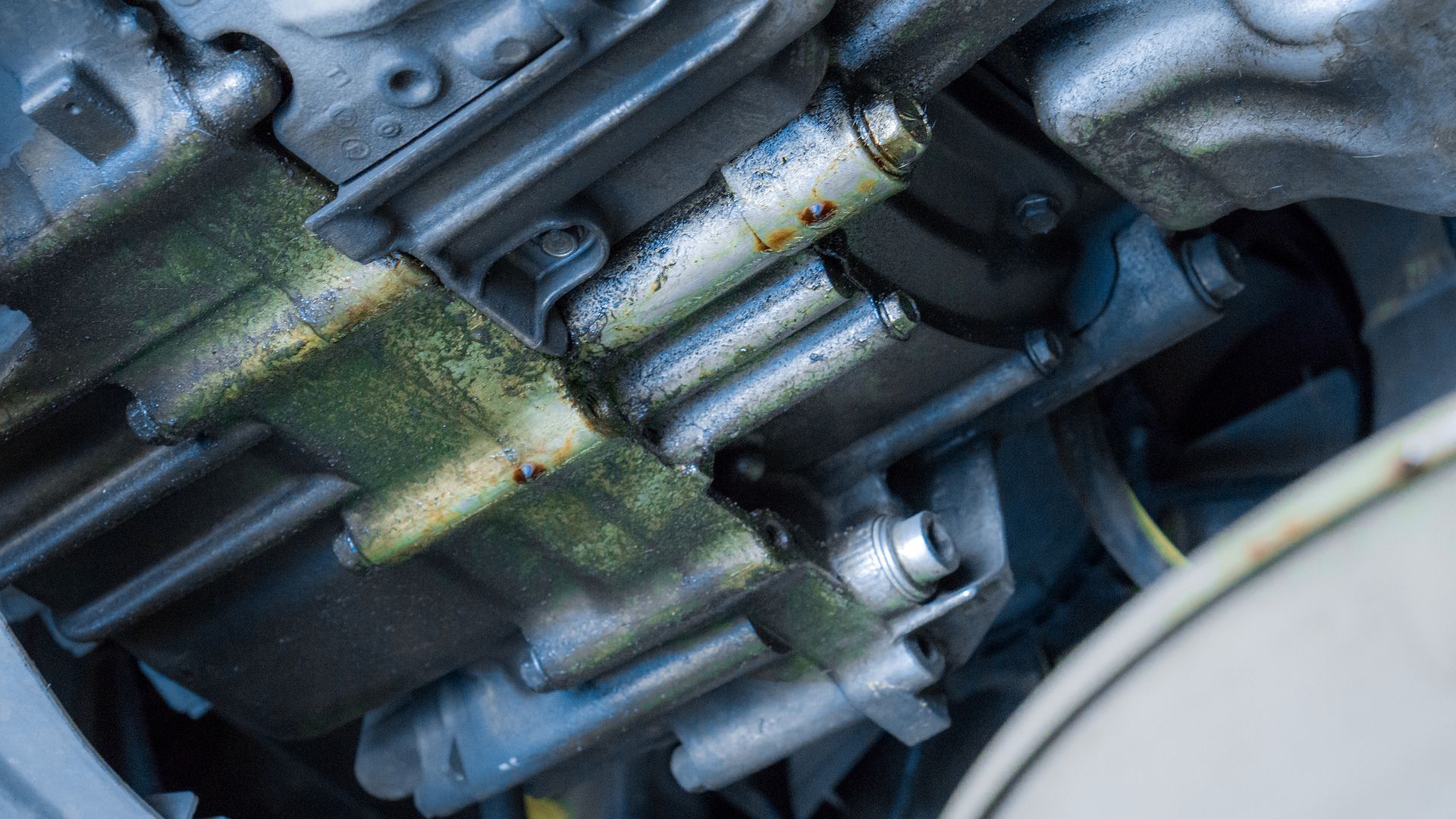 Close-up of a dirty metal engine component with bolts and hoses