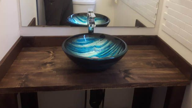 A decorative teal and blue glass vessel sink sits on a dark wooden vanity countertop in a bathroom.