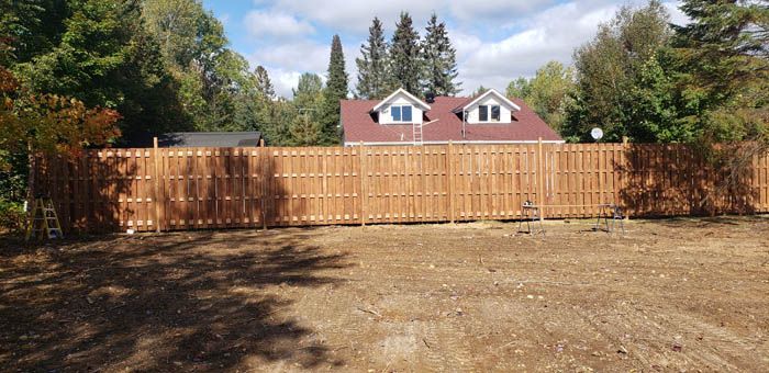 A newly installed wooden fence lines the back of a large, cleared yard, with a house visible in the background.