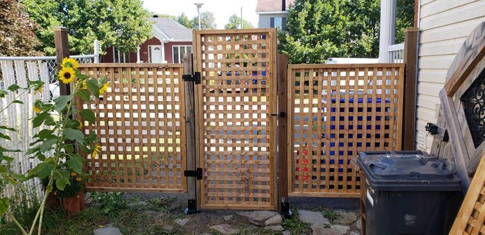 A wooden lattice gate and two matching side panels installed in an outdoor residential space next to a house.