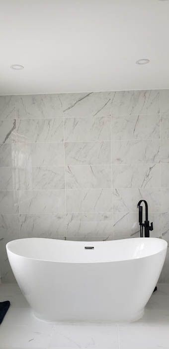 A white freestanding oval bathtub with a black floor-mounted faucet against a grey and white marble-patterned wall.