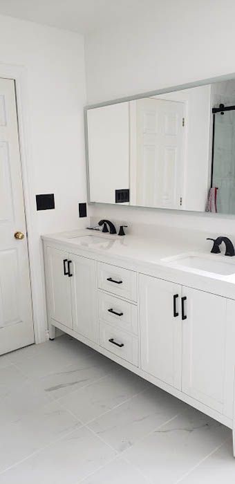 A modern double-sink bathroom vanity with white cabinets, black hardware, and a large mirror against a white wall.