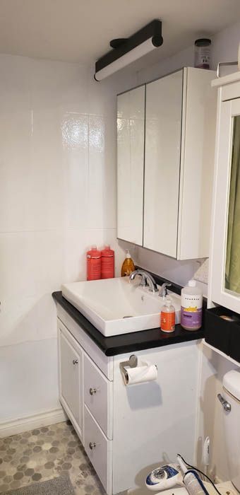 A modern bathroom vanity with a white basin, black countertop, white cabinets, a medicine cabinet, and overhead light.