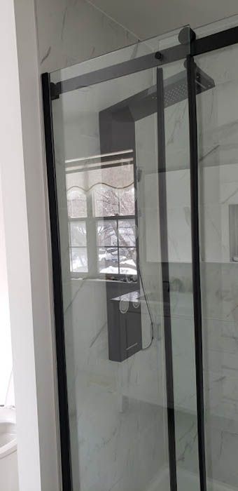 A modern shower enclosure with black-framed sliding glass doors and white tiled walls.