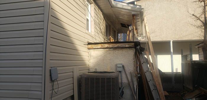 An exterior view of a tan-sided house with a central air conditioning unit and a ladder resting against a porch structure.