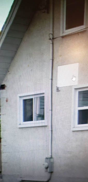 Exterior wall of a house with stucco siding, white window frames, a utility meter at the base, and a vertical conduit.