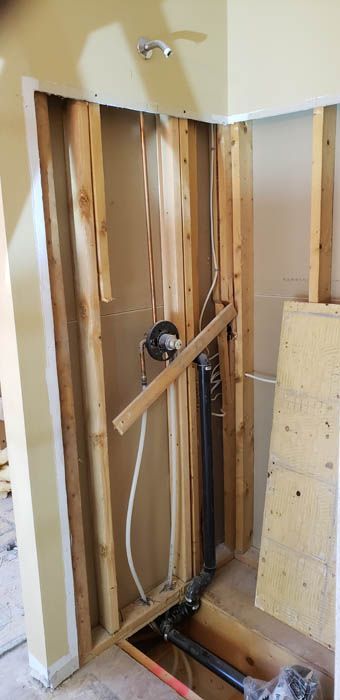 Interior view of a bathroom renovation showing exposed wall studs, plumbing pipes, and a shower valve in an open wall.