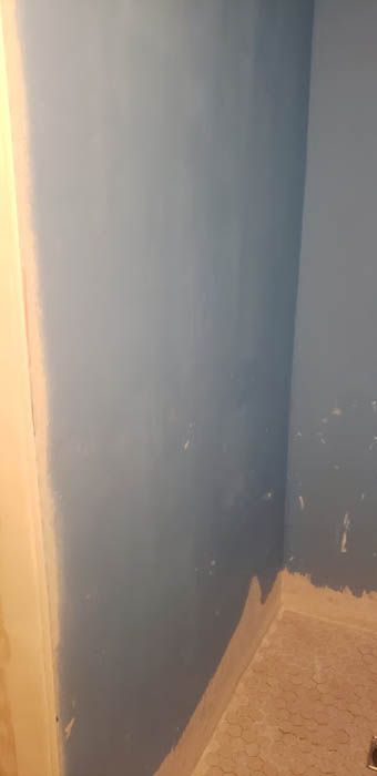 A corner of a room with blue-painted walls meeting an unfinished, light-colored floor base.