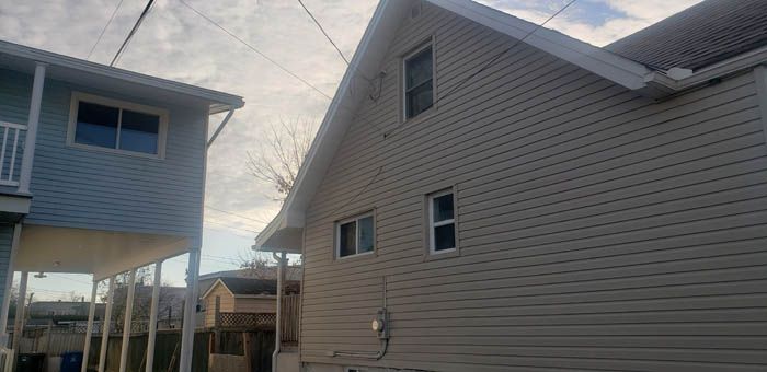 A light blue stilted house stands next to a tan house with white trim on a cloudy day.
